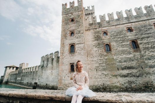 a little girl in a white dress on the background of the old castle in the city of Sirmione.Italy.