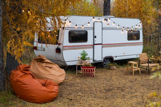 Camper or mobile home in the countryside. Cozy wicker furniture by the van in the autumn forest