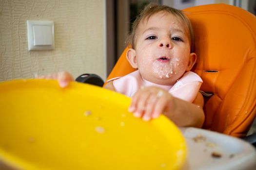 adorable baby plays with plate at the table. little child indulges in a baby chair after eating