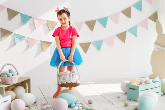 Getting ready to Easter. Lovely little girl holding an Easter egg and smiling with decoration in the background