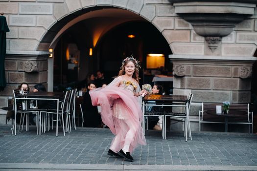 a little girl in a pink Princess dress with a bouquet in her hands walks through the old city of Zurich.Portrait of a girl in a pink dress on a city street in Switzerland.
