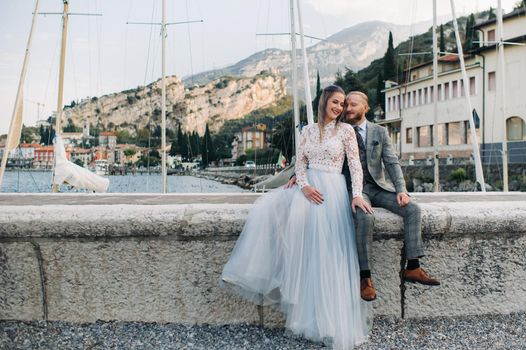 Italy, Lake Garda. A beautiful couple on the shores of lake Garda in Italy at the foot of the Alps.A man and a woman sit on a pier in Italy.