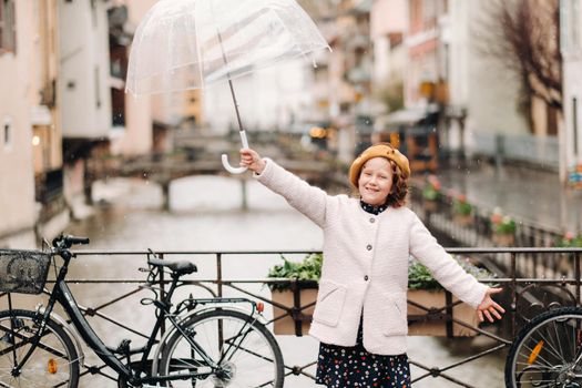 cheerful beautiful girl in a coat with a transparent umbrella in Annecy. France. The girl Cheerfully raises an umbrella in the rain