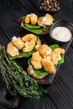 Toasts with Crispy Fried Shrimps Prawns and green salad on a wooden board. Black wooden background. Top view.