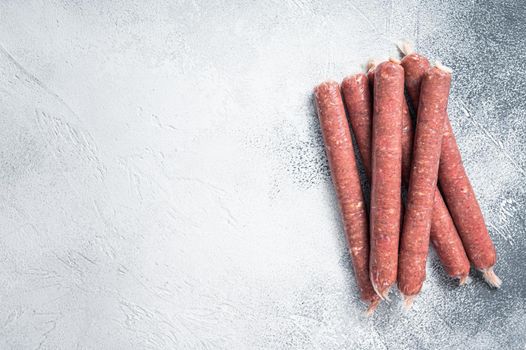 Raw butchers sausages in skins with herbs on kitchen table. White background. Top view. Copy space.