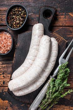 Munich traditional white sausages on a wooden board with thyme. Dark wooden background. Top view.