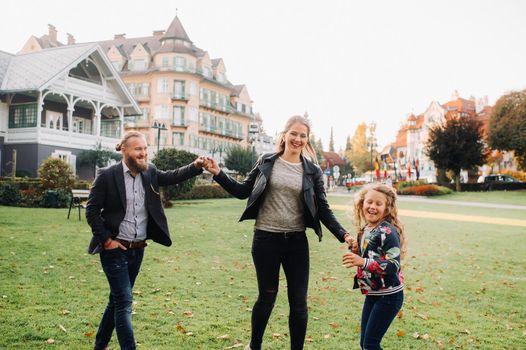 A happy family of three runs through the grass in Austria's old town.A family walks through a small town in Austria.Europe.Velden am werten Zee.