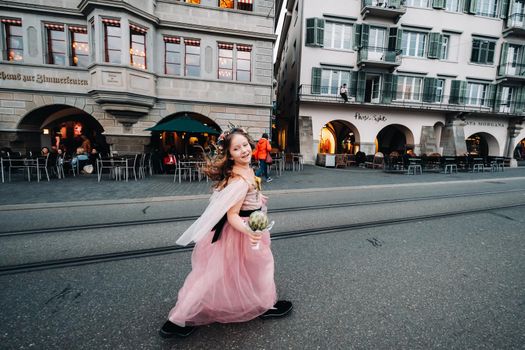 a little girl in a pink Princess dress with a bouquet in her hands walks through the old city of Zurich.Portrait of a girl in a pink dress on a city street in Switzerland.