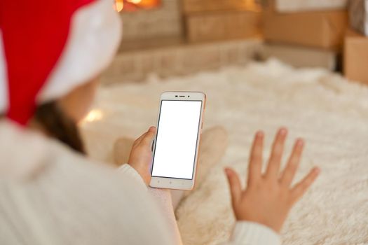 Little girl waves her hand and wishes Happy New Year using mobile phone for video calls, Christmas online holiday, remote celebration X mas in lockdown corona virus.