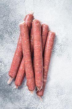 Raw butchers sausages in skins with herbs on kitchen table. White background. Top view.