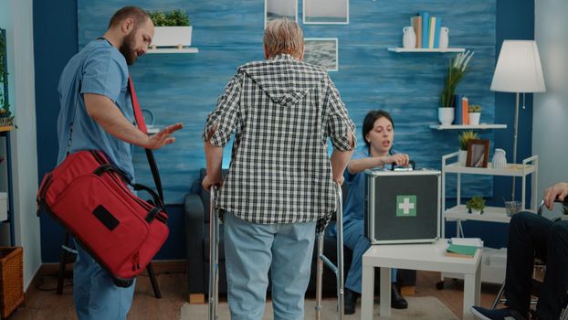 Man nurse supporting senior woman using walk frame at nursing home facility. Medical assistant helping disabled patient walk for recovery. Old person getting help with transportation