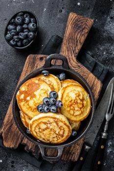 Pancakes with fresh blueberries and maple syrup in a pan. Black background. Top View.