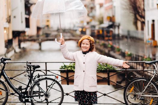 cheerful beautiful girl in a coat with a transparent umbrella in Annecy. France. The girl Cheerfully raises an umbrella in the rain