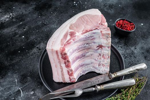 Fresh Raw whole rack of pork loin chops with ribs on a plate with meat fork. Black background. Top view.