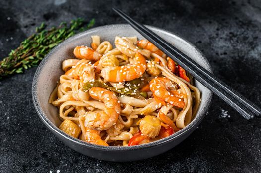 Stir-fry udon seafood noodles with shrimp prawns in a bowl. Black background. Top view.