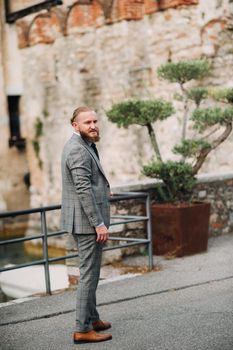 A man with a beard in a strict grey three-piece suit with a tie in the old town of Sirmione, a Stylish man in a grey suit in Italy.