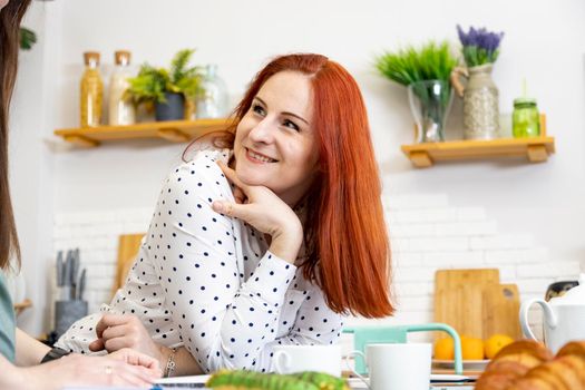 attractive woman with red hair smiling to someone at the kitchen in home interior.