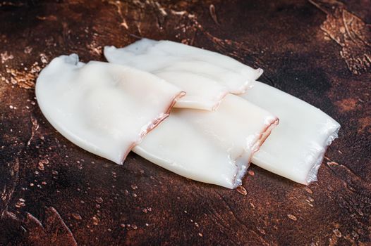 Raw Squid or Calamari tubes on a kitchen table. Dark background. Top view.