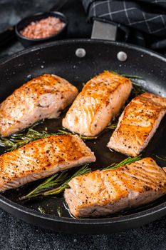 Roasted Salmon Fillet Steak in a pan with rosemary. Black background. Top view.