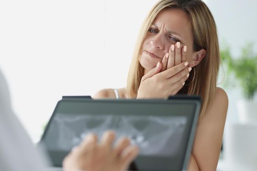 Portrait of woman on dentist appointment in clinic, patient suffer with strong tooth pain. Doctor investigate tooth scan on tablet, x ray result. Healthcare, stomatology concept