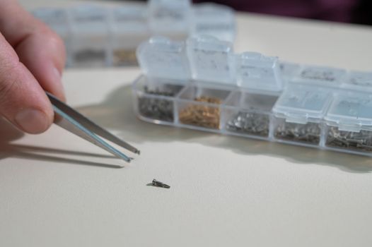 A close-up of male hands takes a screw for repairing glasses with tweezers.