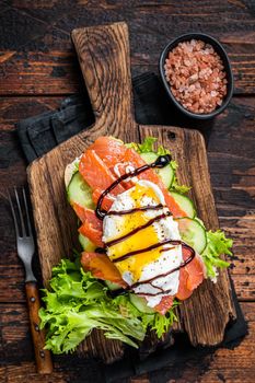 Smoked salmon Sandwich with Benedict egg and avocado on bread. Dark wooden background. Top view.