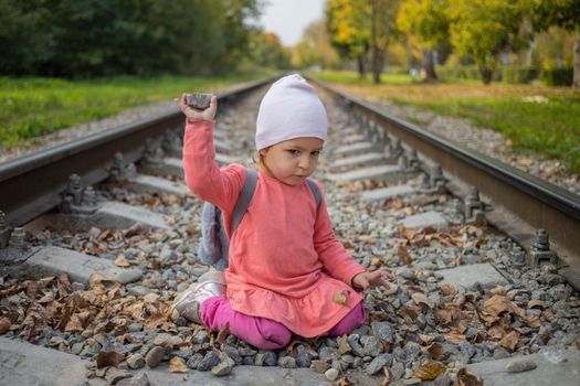 cute toddler girl playing with stones on the railroad embankment. dangerous games