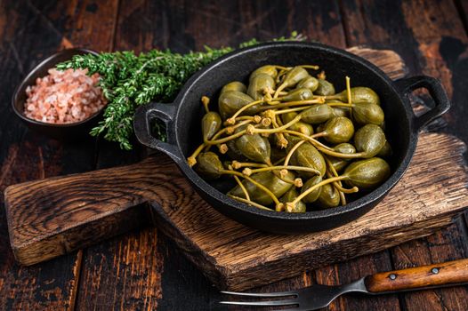 Marinated canned capers in a pan. Dark wooden background. Top view.