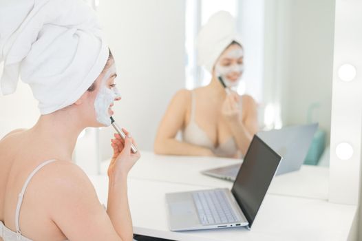 Caucasian woman applying face mask and looking at laptop manual