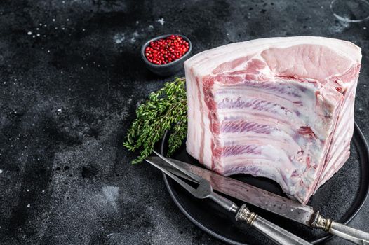 Fresh Raw whole rack of pork loin chops with ribs on a plate with meat fork. Black background. Top view. Copy space.