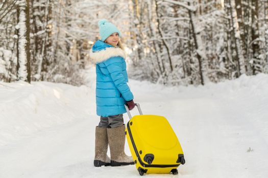 A girl in winter in felt boots goes with a suitcase on a frosty snowy day.