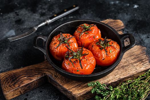 Roasted cherry tomatoes with thyme in a pan. Black background. Top view.