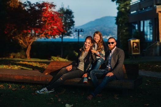 A happy family of three sits on a bench at a Sunny autumn sunset in Austria's Old town.A family poses in a small Austrian town against the backdrop of the Austrian Alps.Europe.Felden am see.