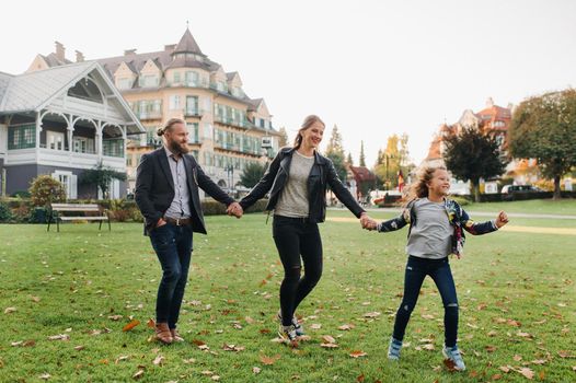 A happy family of three runs through the grass in Austria's old town.A family walks through a small town in Austria.Europe.Velden am werten Zee.