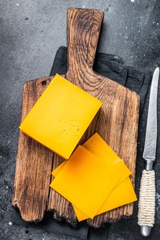 Slices of Cheddar Cheese on a wooden cutting board. black background. Top view.