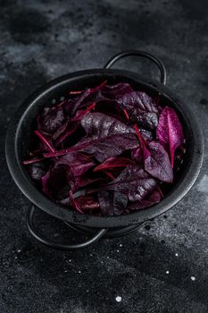 Leaves of Swiss red chard or Mangold salad in a colander. Black background. Top view.