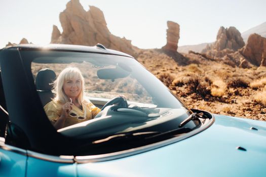 Girl in yellow dress enjoying a road trip in a convertible through a deserted valley with mountains, Canary Islands, Tenerife