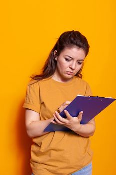 Young person taking notes on notebook files with pen in studio. Concentrated woman writing on textbook papers, signing documents and paperwork about project on notepad clipboard.