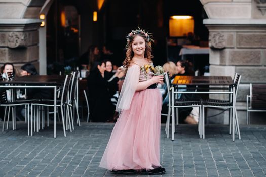 a little girl in a pink Princess dress with a bouquet in her hands walks through the old city of Zurich.Portrait of a girl in a pink dress on a city street in Switzerland.