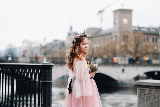 a little girl in a pink Princess dress with a bouquet in her hands walks through the old city of Zurich.Portrait of a girl in a pink dress on a city street in Switzerland.