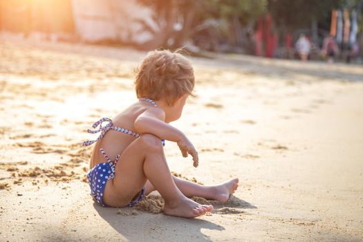 portrait of little girl sitting on a sandy beach in the sun