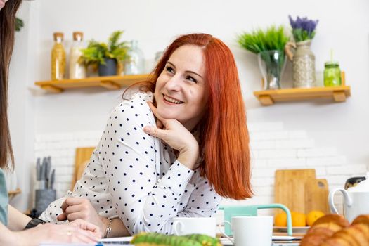 portrait of attractive woman with red hair talking to someone at the kitchen at home and smiling sincerely.