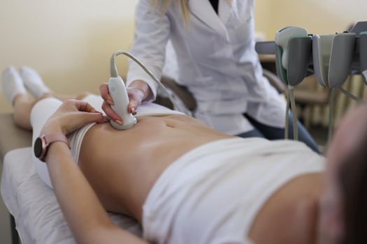 Close-up of gynecologist doing ultrasound scan in modern clinic, doctor in white lab coat examining woman. Female patient expecting pregnancy. Medicine, gynecology, health concept