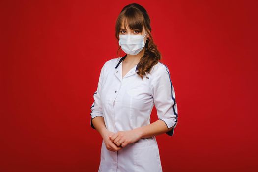 A female doctor stands in a medical mask isolated on a red background