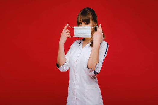 A female doctor stands in a medical mask isolated on a red background