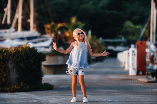 Cute girl near the yachts in the summer. Travel, adventure, boat trips with a child for a family vacation. Children's clothing in the style of a sailor, marine fashion