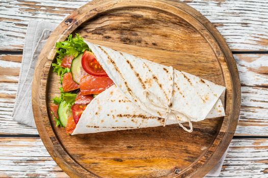 Wrap salmon sandwich, roll with fish and vegetables. White wooden background. Top view.