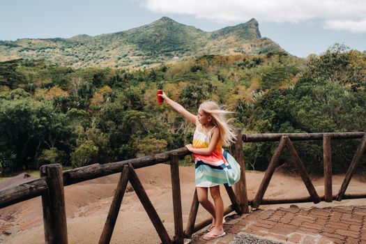 a little girl with a red can of drink in her hands against the background of the mountains of the island of Mauritius, nature reserve, Chamarel Sands.Mauritius island.