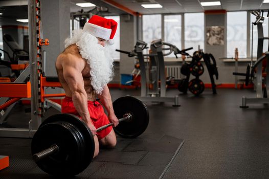 Santa claus in the gym. Muscular man with a naked torso doing exercises with dumbbells