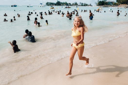 a little girl runs along a tropical beach with locals on the island of Mauritius.a girl on the beach of the Indian ocean and unrecognizable locals of the island of Mauritius.